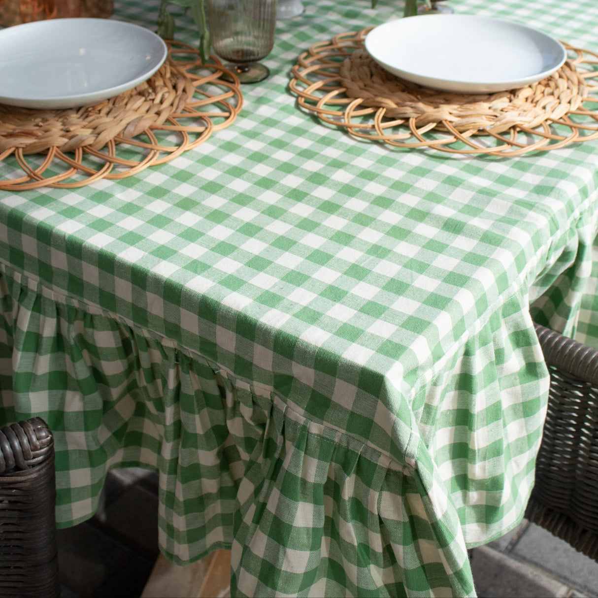 Table setting with green and white checkered tablecloth, wicker chargers, and floral centerpieces.