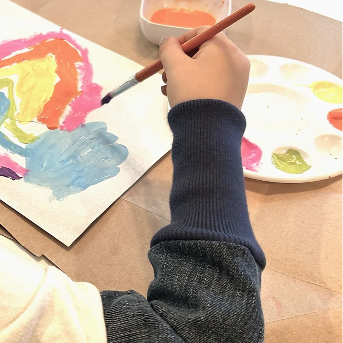 Person painting with watercolors on a piece of paper, using a brush and a small container of paint.