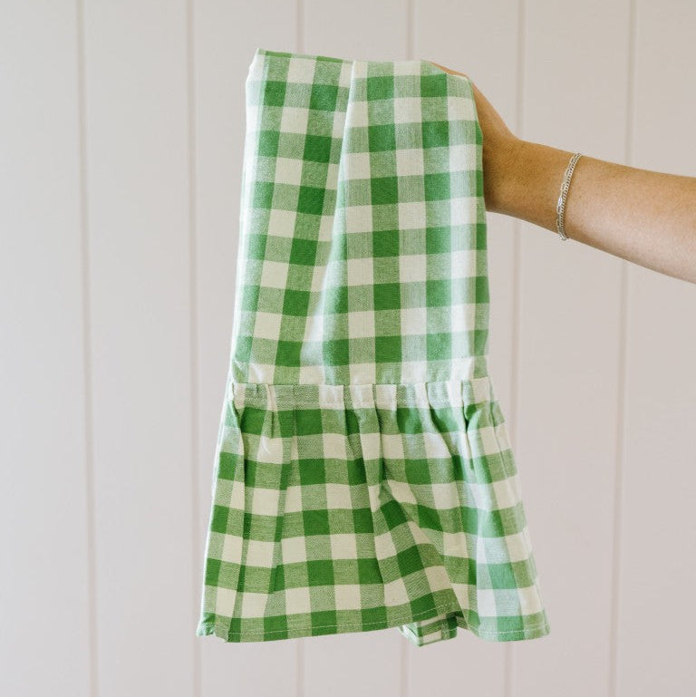 Green and white checkered dress held by a person against a white wooden panel background