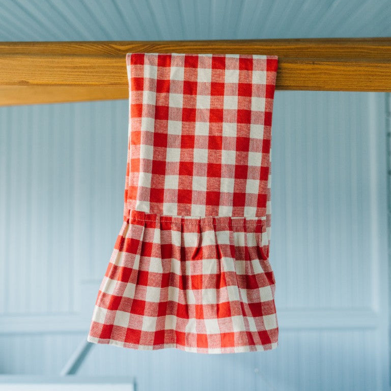 Red and white checkered dress hanging on a wooden rod against a light blue wall.