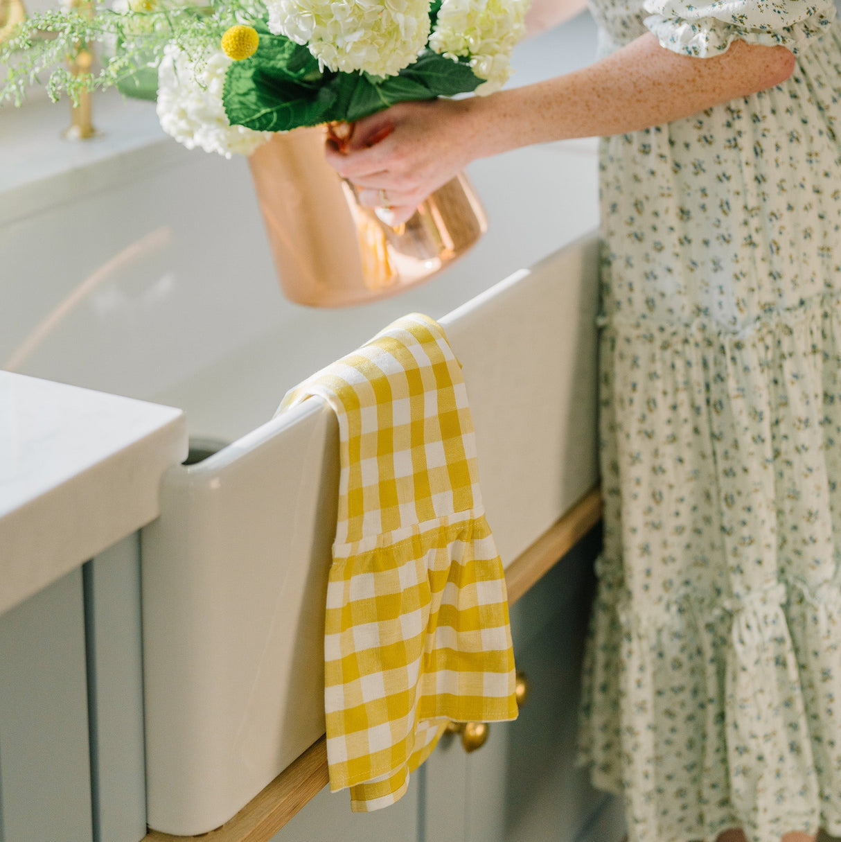 Person holding a bouquet of flowers in a kitchen with a yellow towel on the sink.