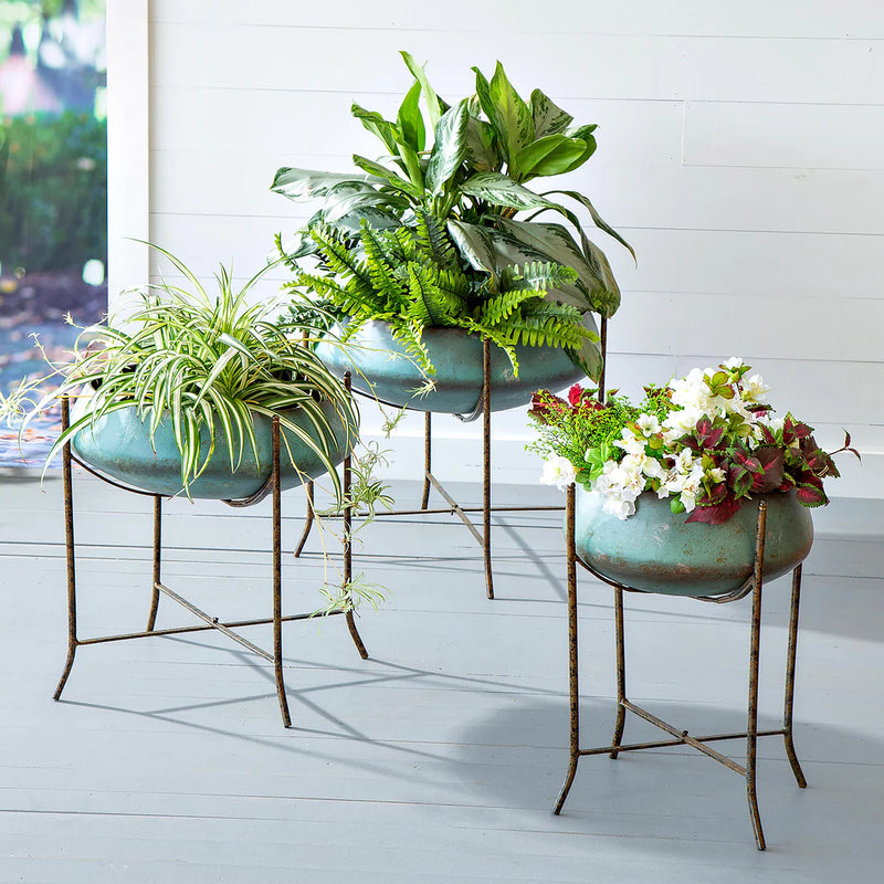 Three decorative planters with plants on stands against a white wall