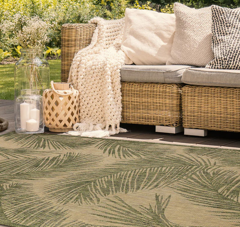 Wicker outdoor furniture with cushions and a blanket on a patio with a leaf-patterned rug.