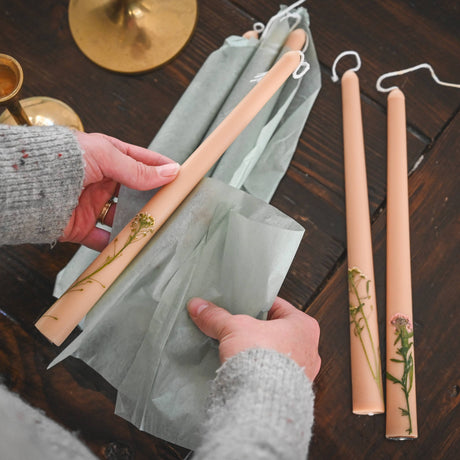 Person holding a set of wooden candles with green paper on a wooden surface