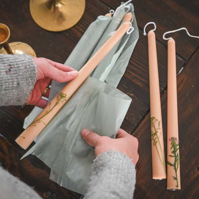 Person holding a set of wooden candles with green paper on a wooden surface
