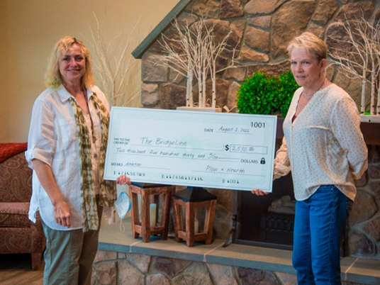 Pictured: BridgeLine Executive Director Daniela Pretzer (left) accepts the donation from Leslie Newton, President Plow & Hearth | Evergreen