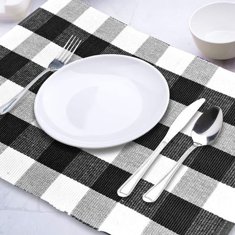Dinner setting with a black and white checkered placemat, white plate, silver fork, knife, and spoon on a light gray surface.
