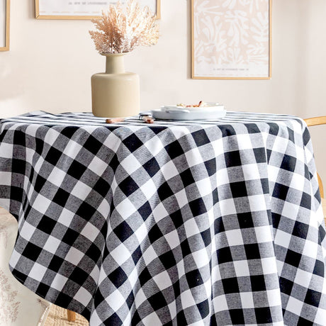 Black and white checkered tablecloth on a round table with a vase and plates in a room.