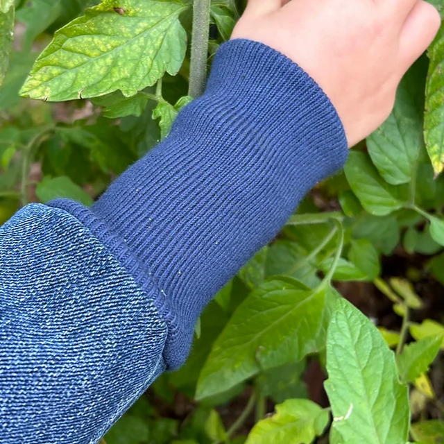 Hand picking a tomato from a plant with a blue sleeve