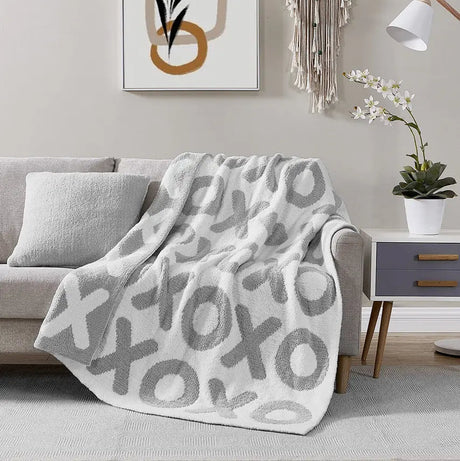 Gray patterned blanket draped over a gray sofa in a living room setting.